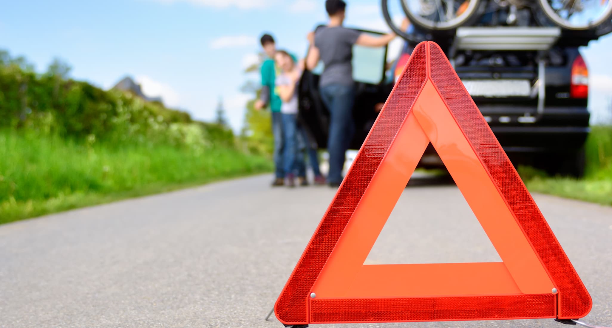 A warning triangle in front of a car that has broken down.