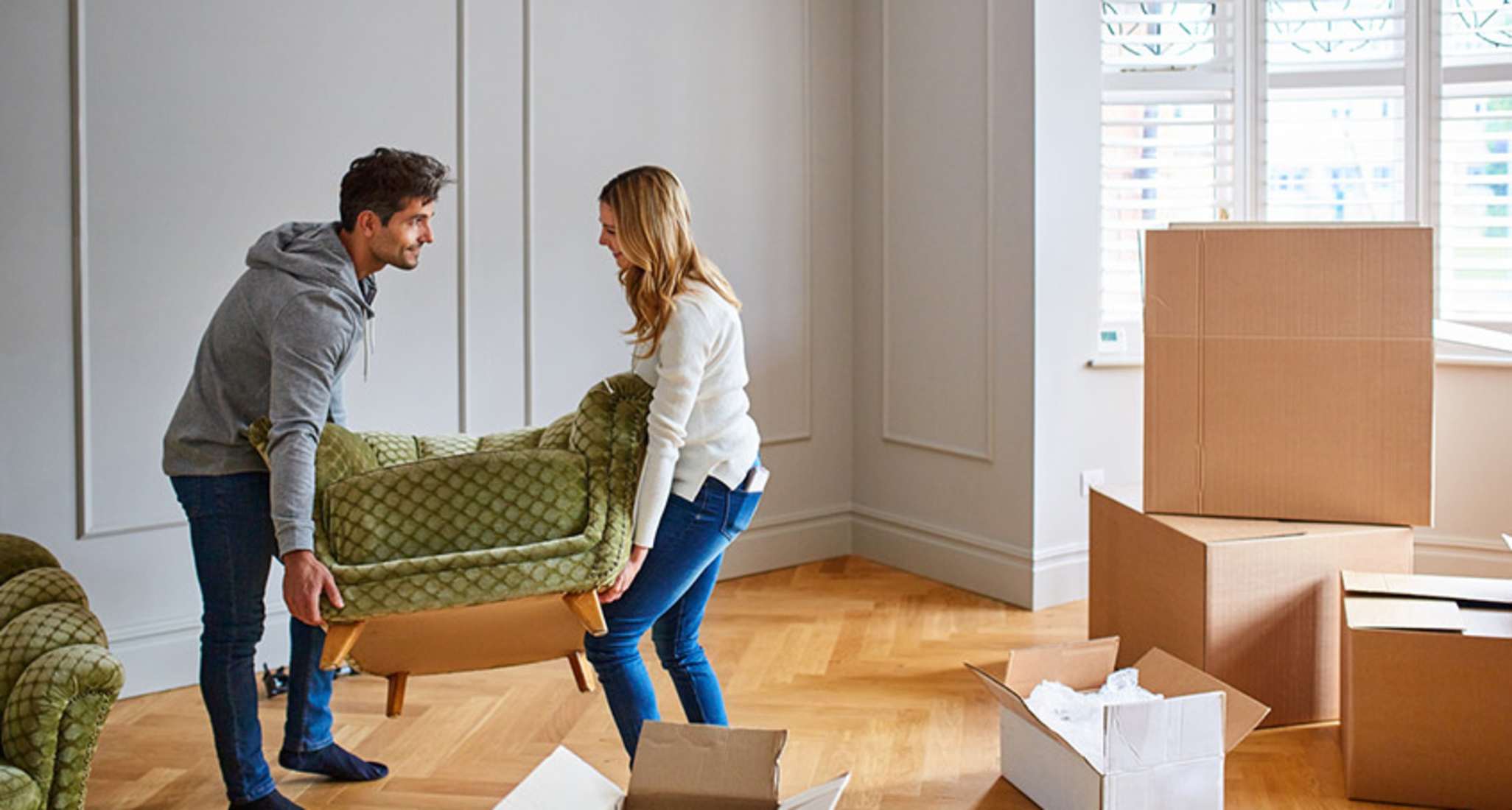 Couple moving armchairs around in a new apartment, surrounded by moving boxes.