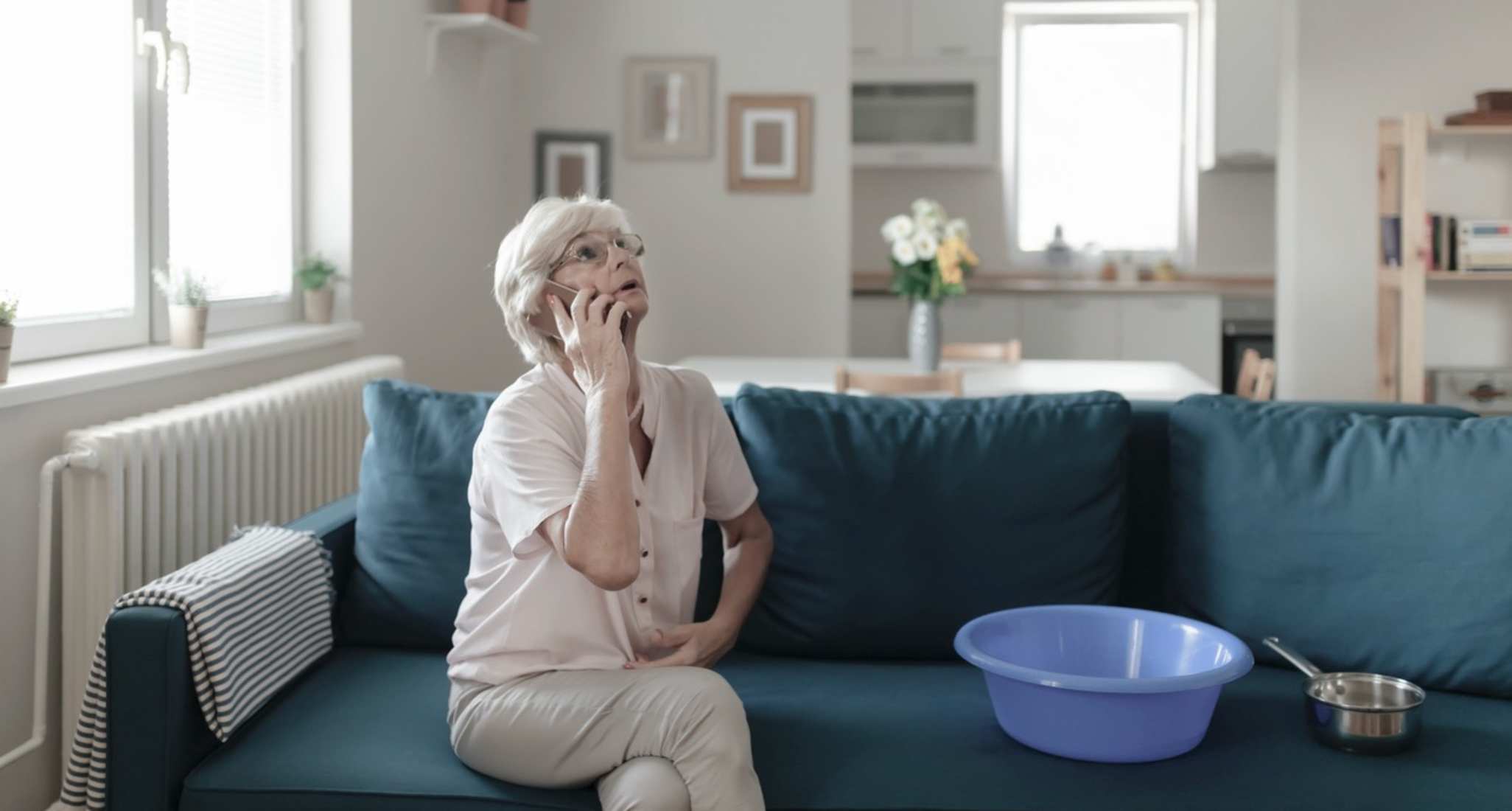 Eine alte Frau telefoniert auf dem Sofa, während sie versucht, einen Wasserschaden in den Griff zu bekommen.