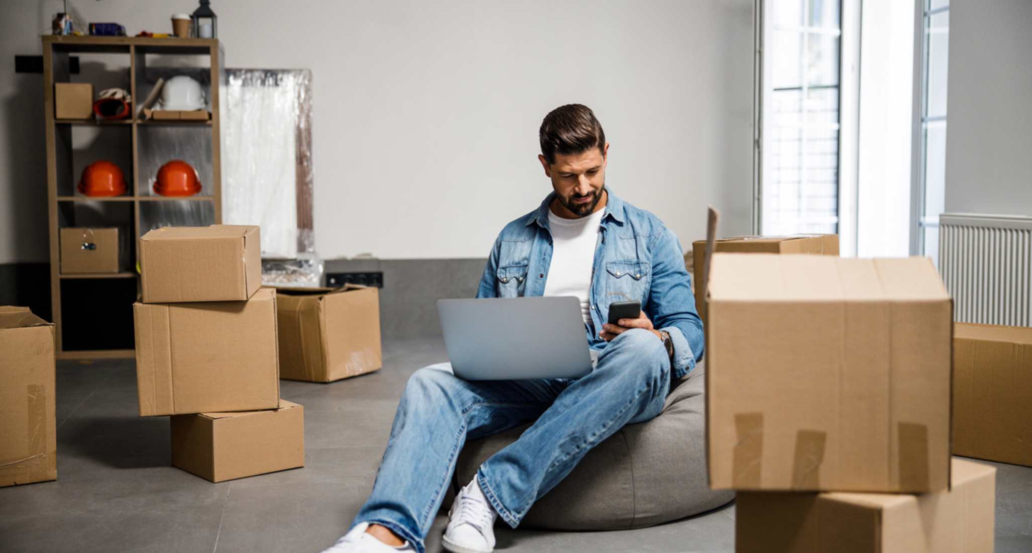 A young man with a laptop and moving boxes
