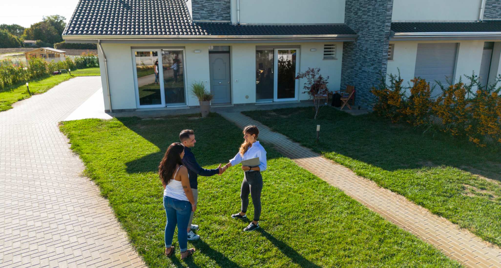 Una coppia e un agente immobiliare davanti a una casa.