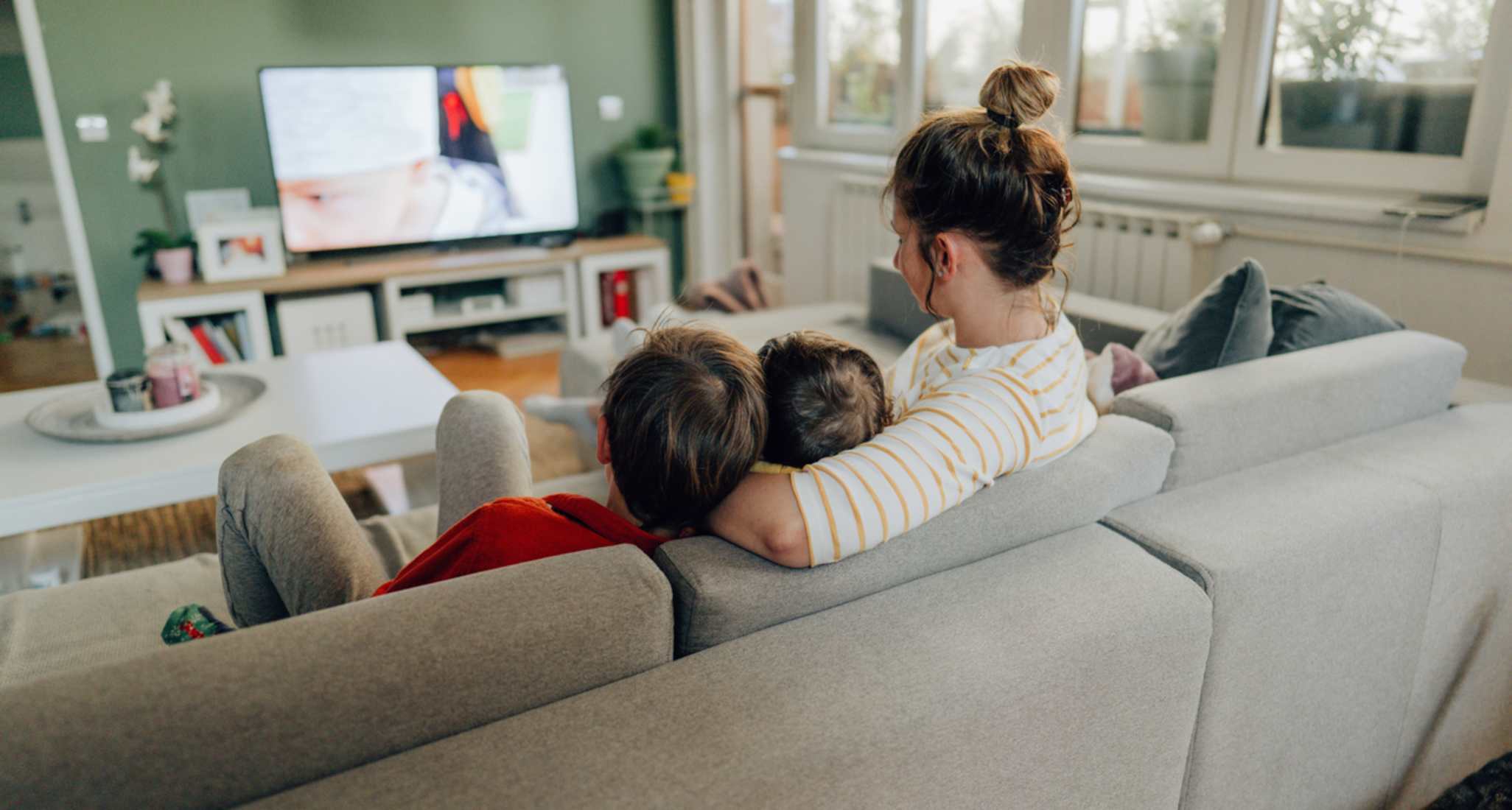Une famille est assise sur le canapé. Le téléviseur diffuse un film ou une série via un service de streaming.