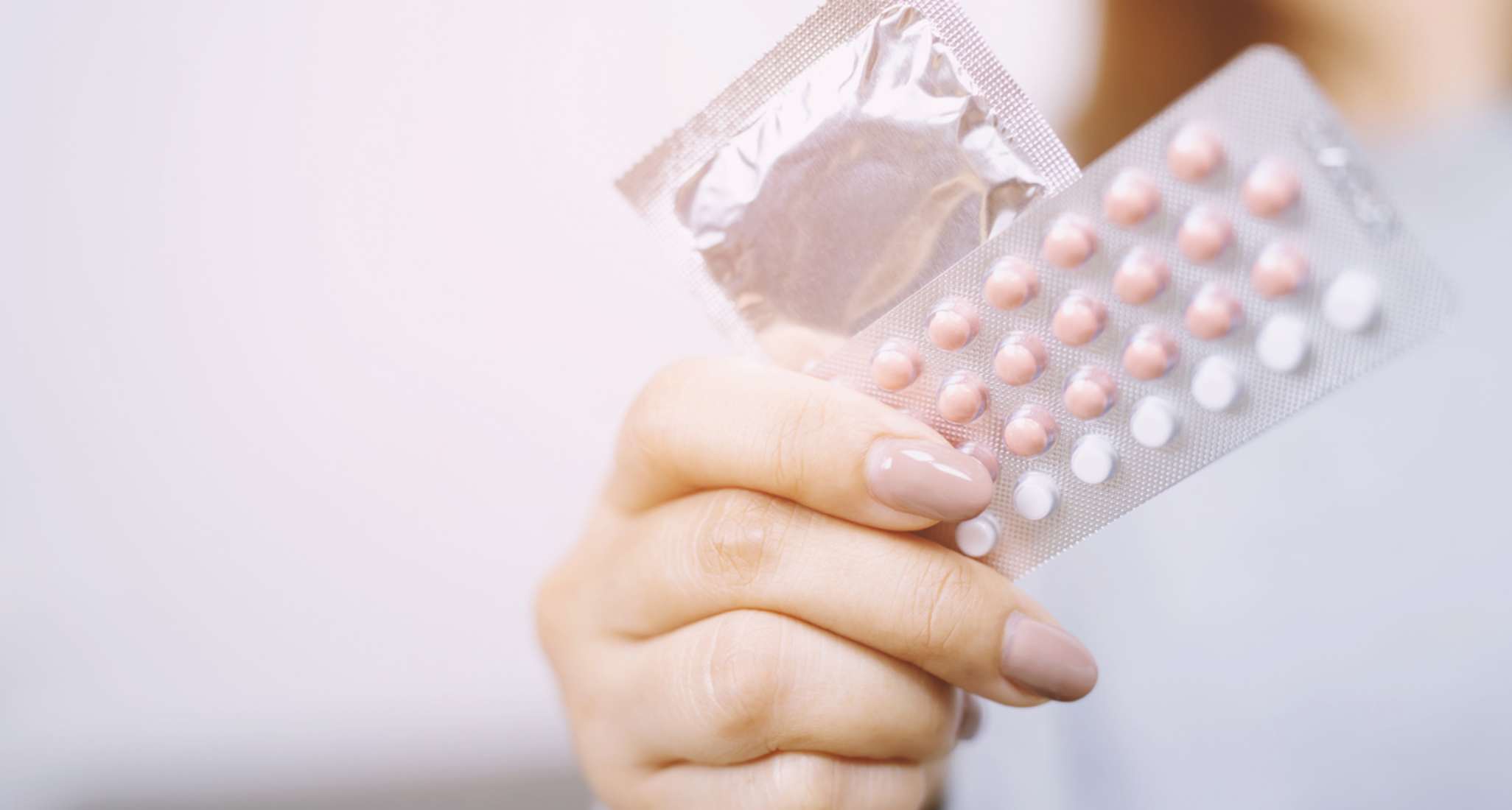 Hand holding a condom and a pack of pills