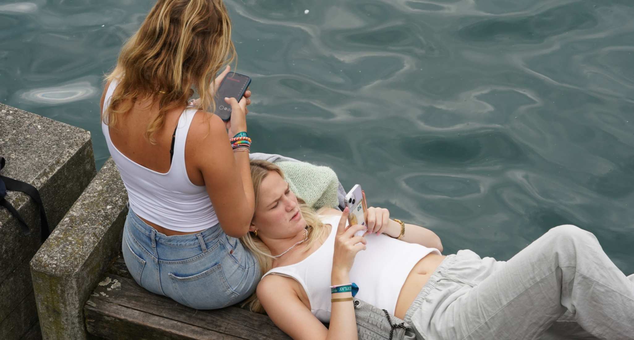 Due donne sono sedute su una panchina sul Lago di Zurigo. Entrambe guardano il proprio smartphone.
