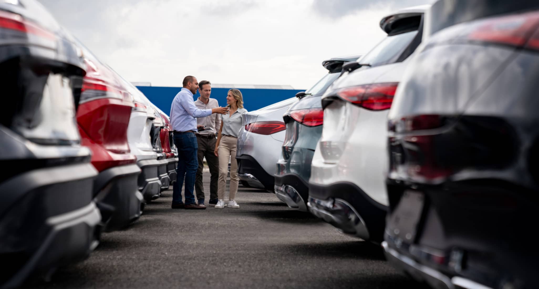 Ein Verkäufer zeigt einem Pärchen verschiedene Occassionsautos, die zum Verkauf stehen.