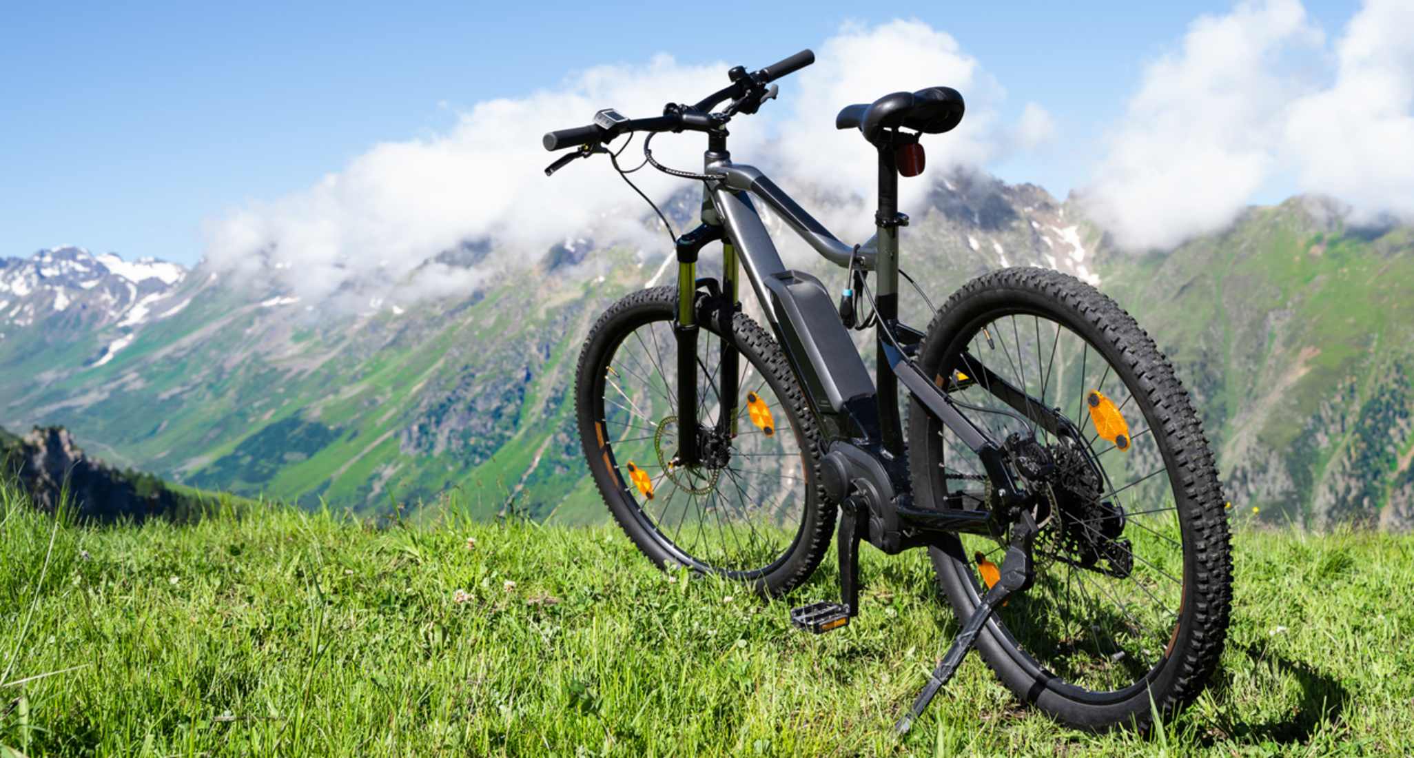 Ein E-Bike steht auf einer Wiese. Im Hintergrund sind Berge zu sehen.