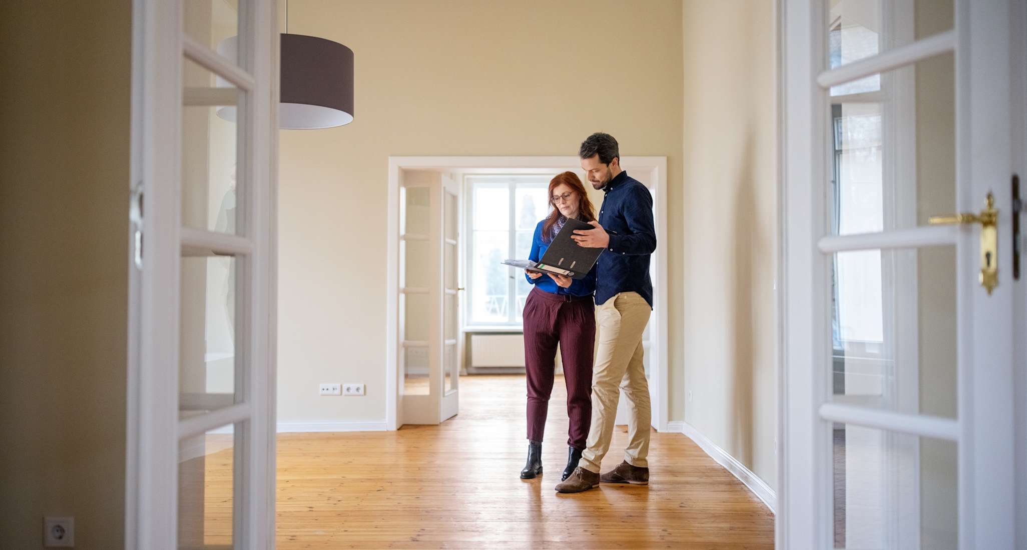 Kaufinteressiertes Paar prüft in einer leeren Wohnung die Unterlagen zur Immobilie.
