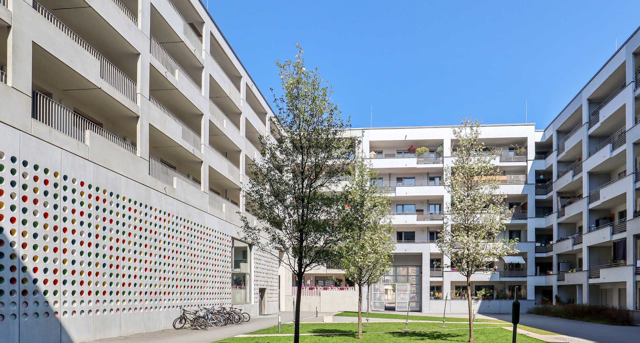 Begrünter Innenhof einer modernen Wohnsiedlung mit Mehrfamilienhäusern und Veloabstellplatz.