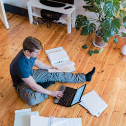 Ein junger Mann erledigt am Boden sitzend seine Steuererklärung.