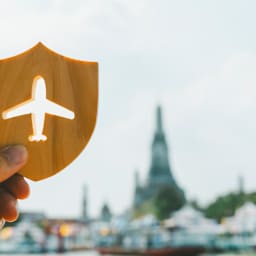 Eine Hand hält ein kleines Schild aus Holz, aus dem ein Flugzeug ausgeschnitten ist.
