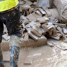 Eine Person vor schlammigem Hausrat nach einem Hochwasser.