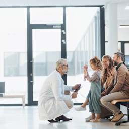 Eine Familie im Wartezimmer eines Krankenhauses. Ein Arzt hockt vor der stehenden jungen Tochter.