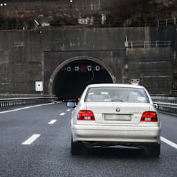 A silver car with a Fribourg number plate is driving towards a tunnel.