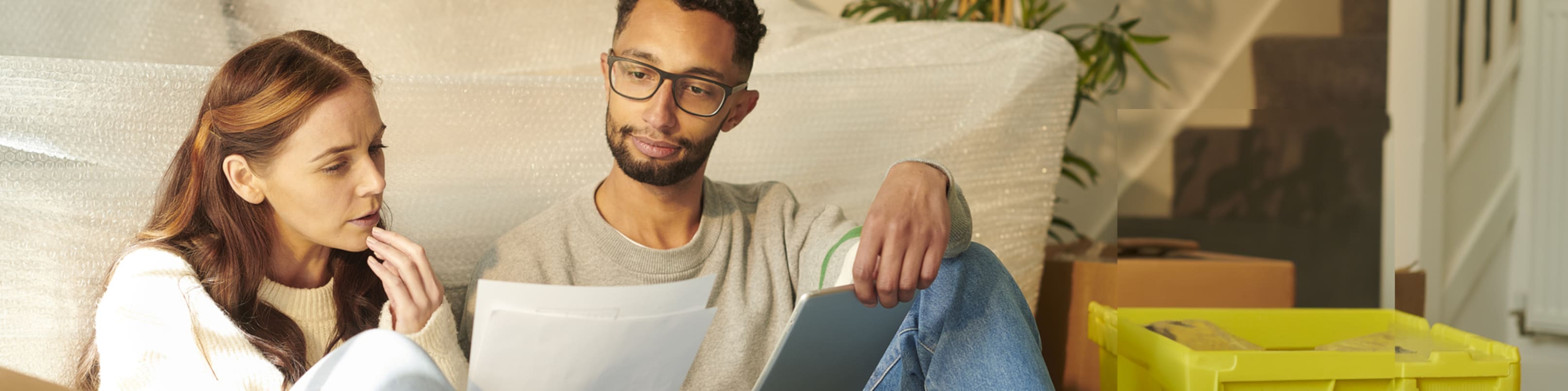 Ein Paar sitzt vor noch eingepackten Möbeln in ihrer neuen gemeinsamen Wohnung.