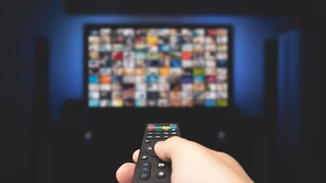 Une personne pointe une télécommande vers un téléviseur. L’écran est couvert de petites images.