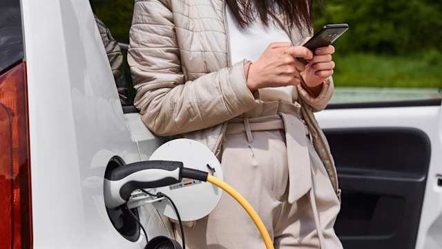 A woman standing next to a charging electric car.