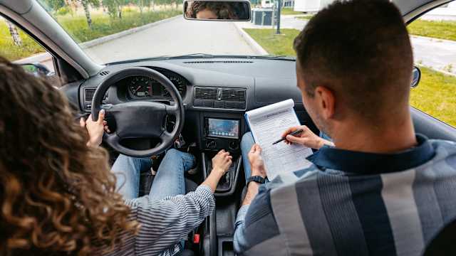 Eine junge Frau bei ihrer Fahrprüfung. Neben ihr sitzt ein Prüfer.