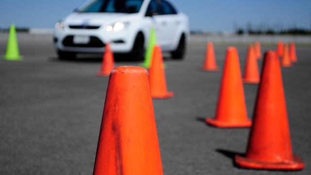 Weisses Auto auf Fahrübungsplatz mit orangen Strassenverkehrs-Hütchen im Vordergrund