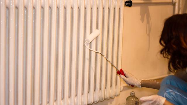 Une femme peint son radiateur.