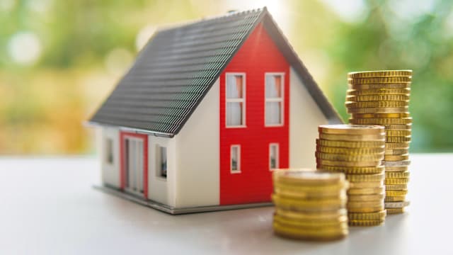 Miniature house with a pile of coins in the foreground