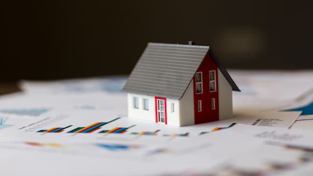 Modell eines Einfamilienhauses steht auf ausgedruckten Finanzdiagrammen.