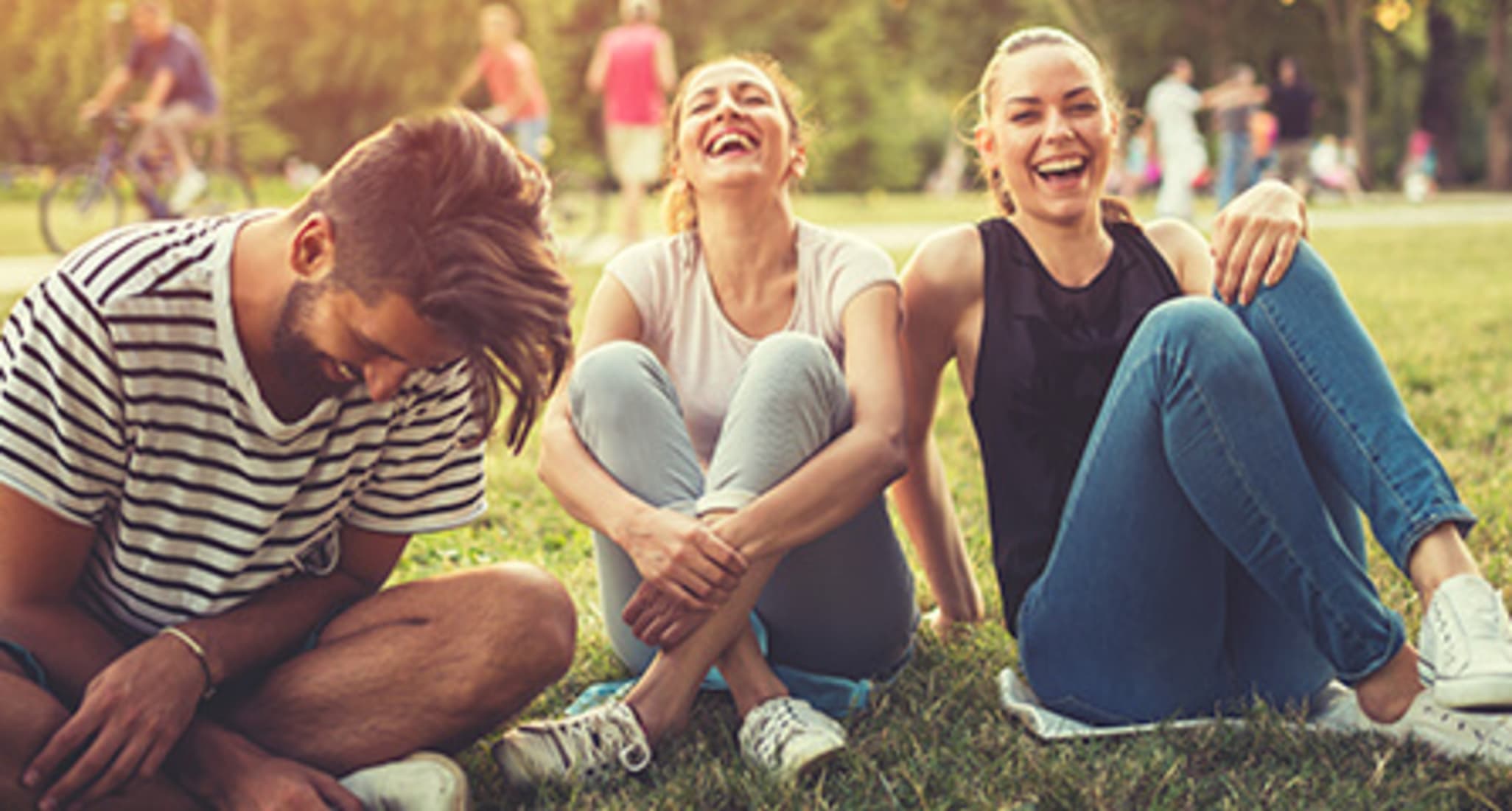 A group of young people are sitting on the grass, laughing. 