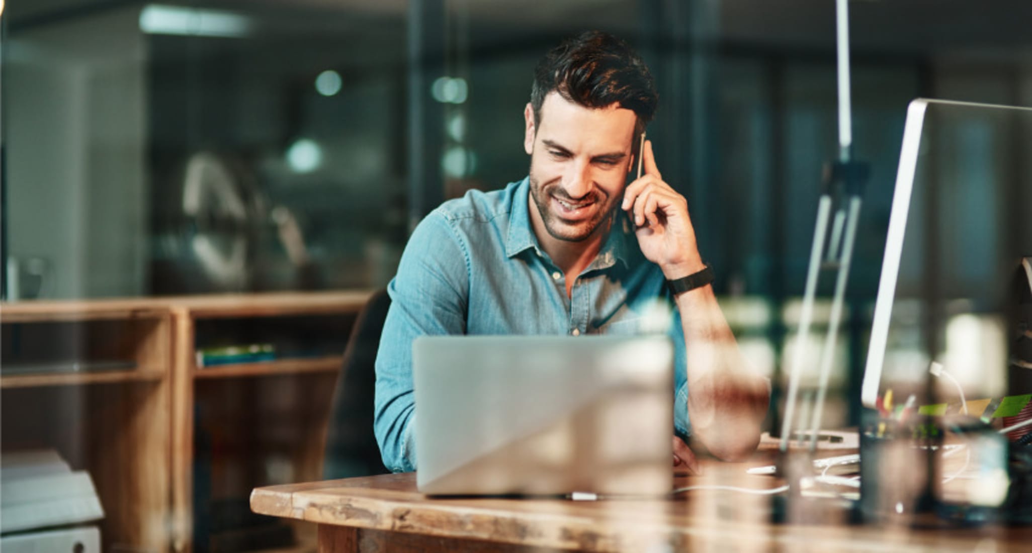 Un uomo di 38 anni è seduto davanti al portatile ed è al telefono. Vuole sapere come procedere se vuole acquistare un appartamento di proprietà come investimento.