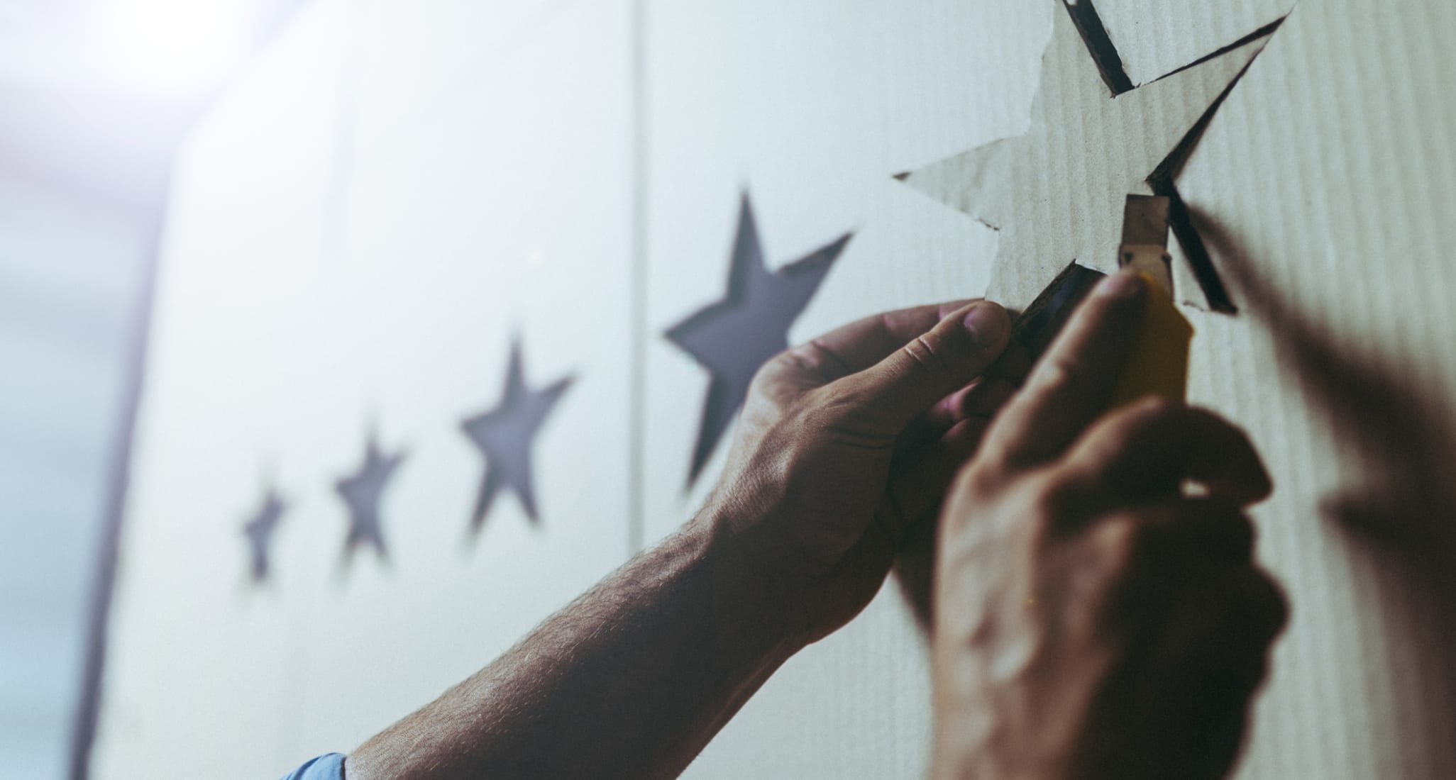 A man cuts a star shape out of cardboard using a utility knife. To the left of it, four other stars have already been cut out.