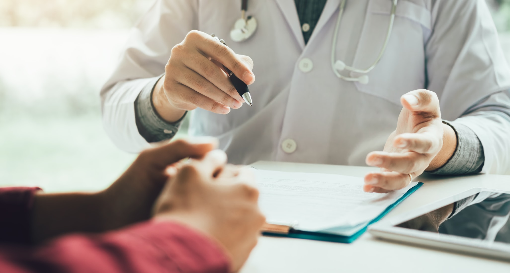 A doctor with a pen in his hand discusses life insurance with a patient.