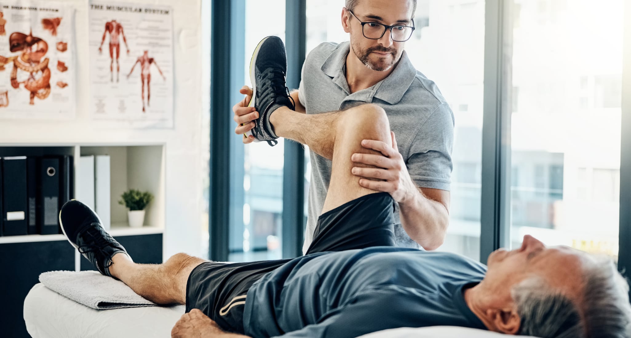 A physiotherapist bending an older man's leg.