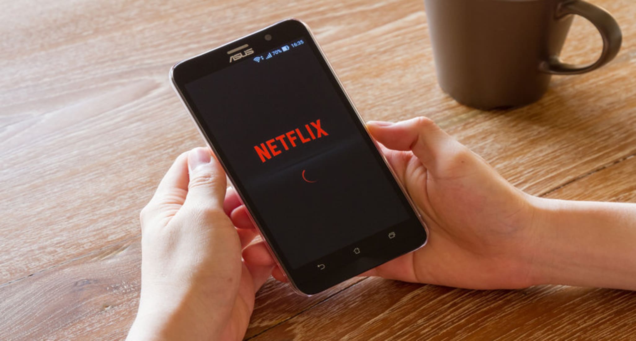 Someone with a smartphone in their hands and a cup of coffee to the right. The Netflix app is open. The streaming service has been operating in Switzerland since 2014.