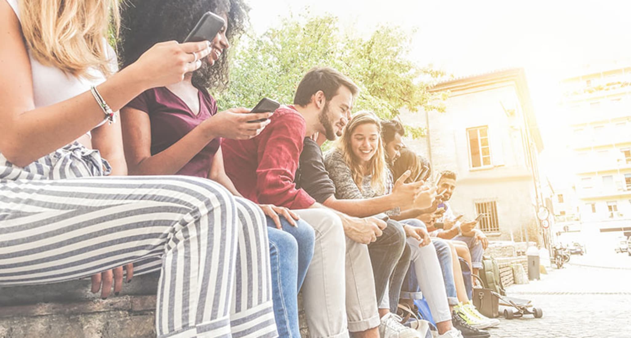 Junge Frauen und Männer sitzen nebeneinander und nutzen ihre Smartphones. 