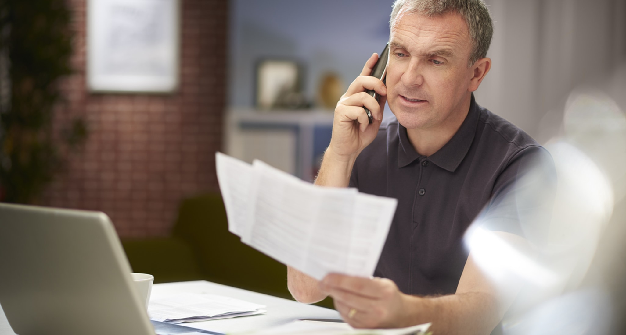 A man is on the phone, holding various documents in his hand.