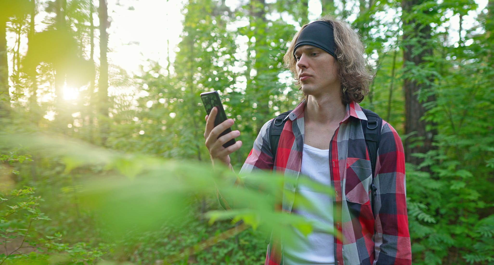 A man with a smartphone standing in the woods. 