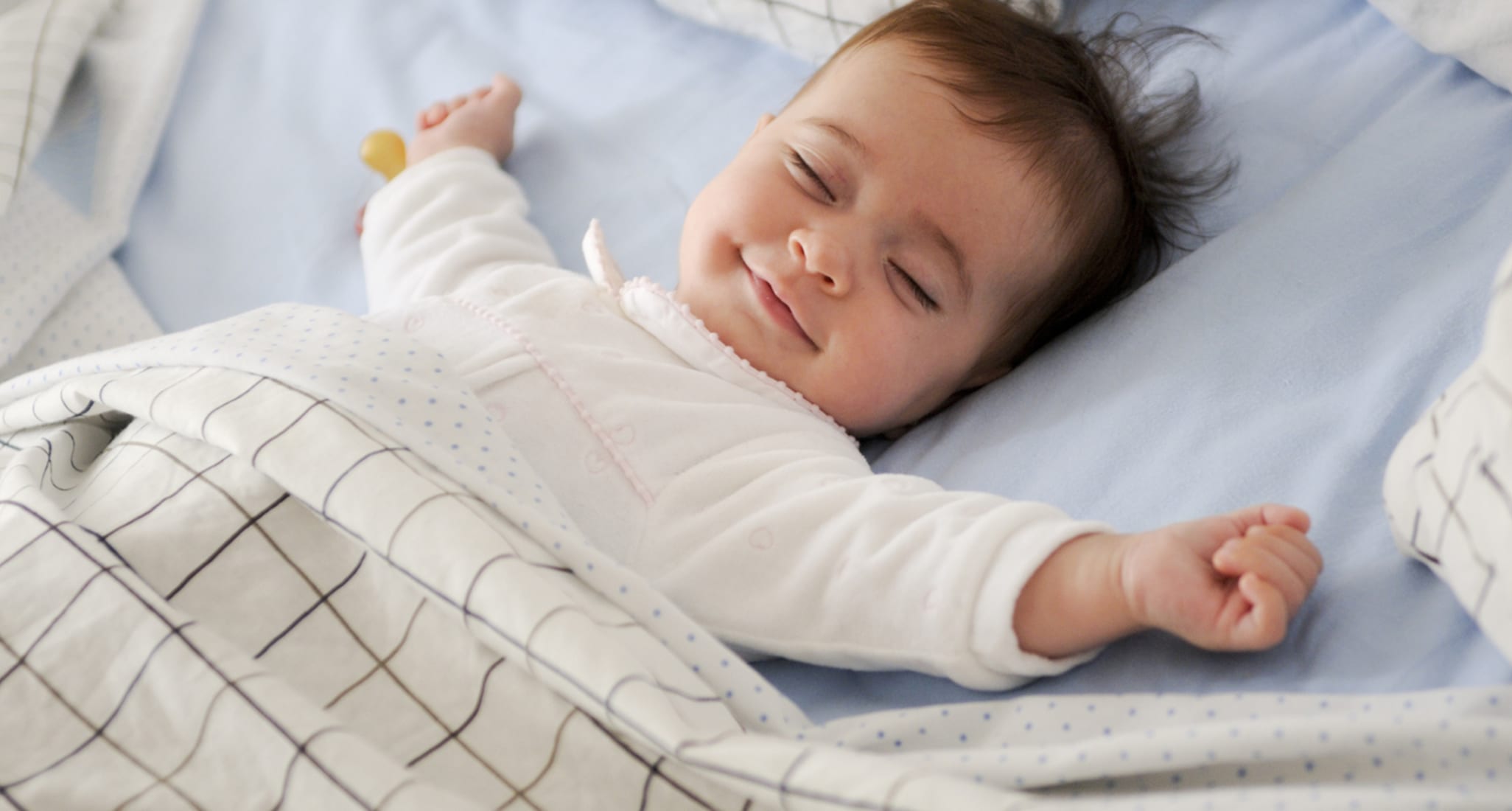 Un bambino disteso sul letto dorme sorridendo.