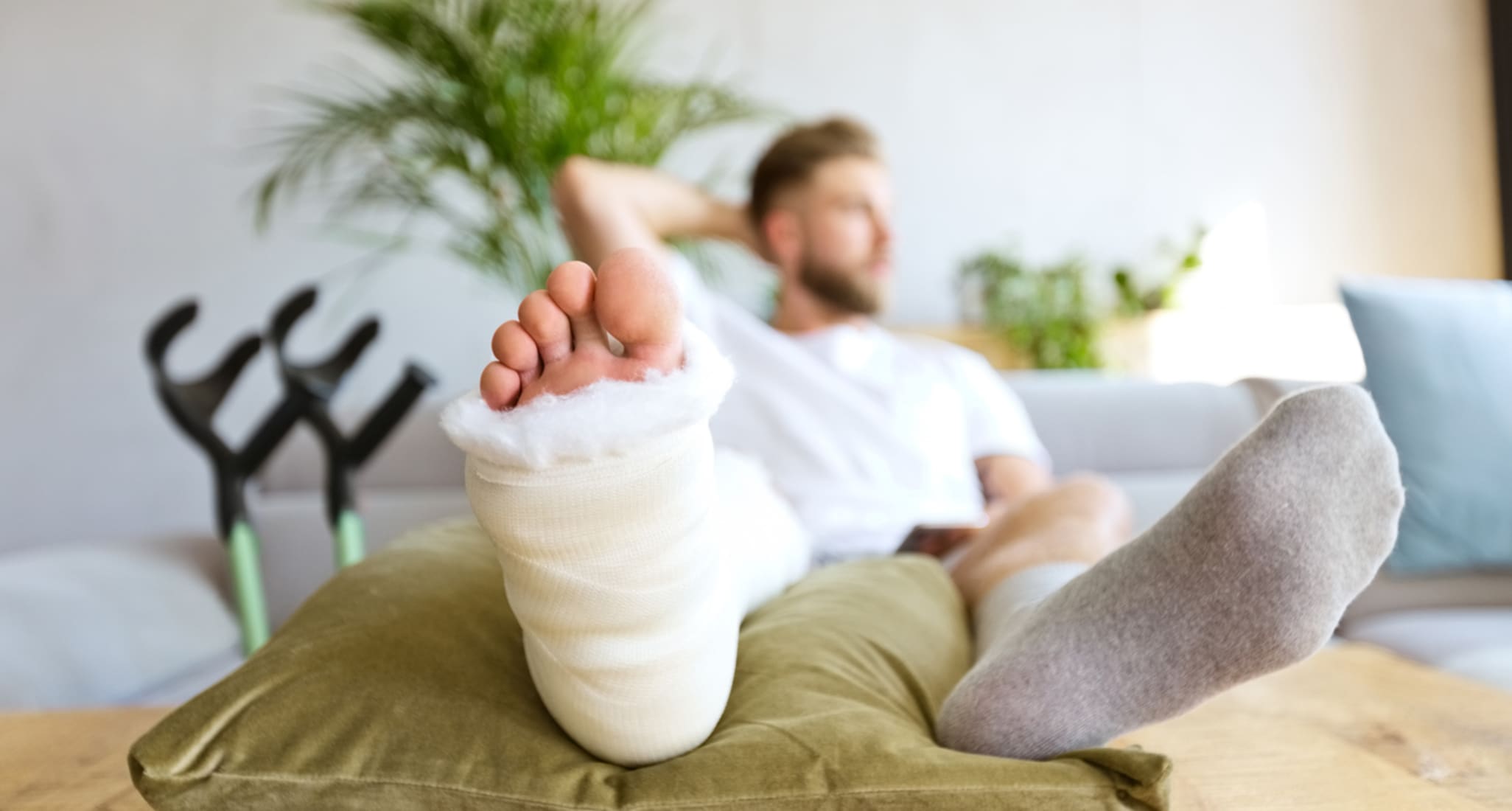 Ein junger Mann mit gebrochenem Fuss sitzt auf dem Sofa.