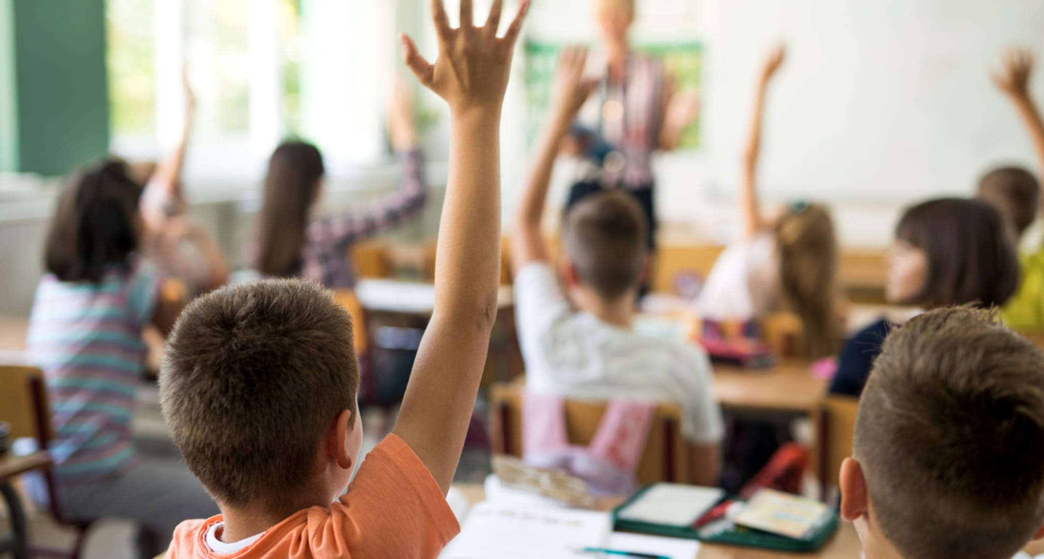 En classe, un petit garçon et ses camarades lèvent la main pour répondre à la question de l’enseignant pendant le cours.