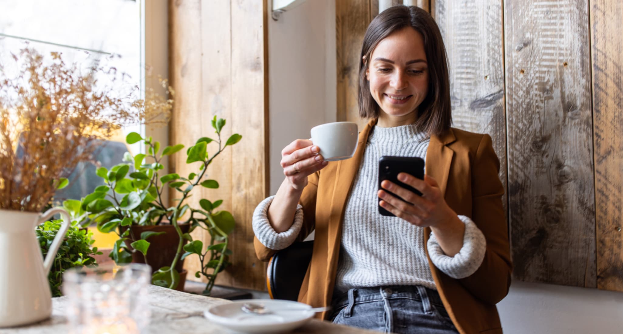 Una giovane donna beve caffè e usa il suo smartphone.