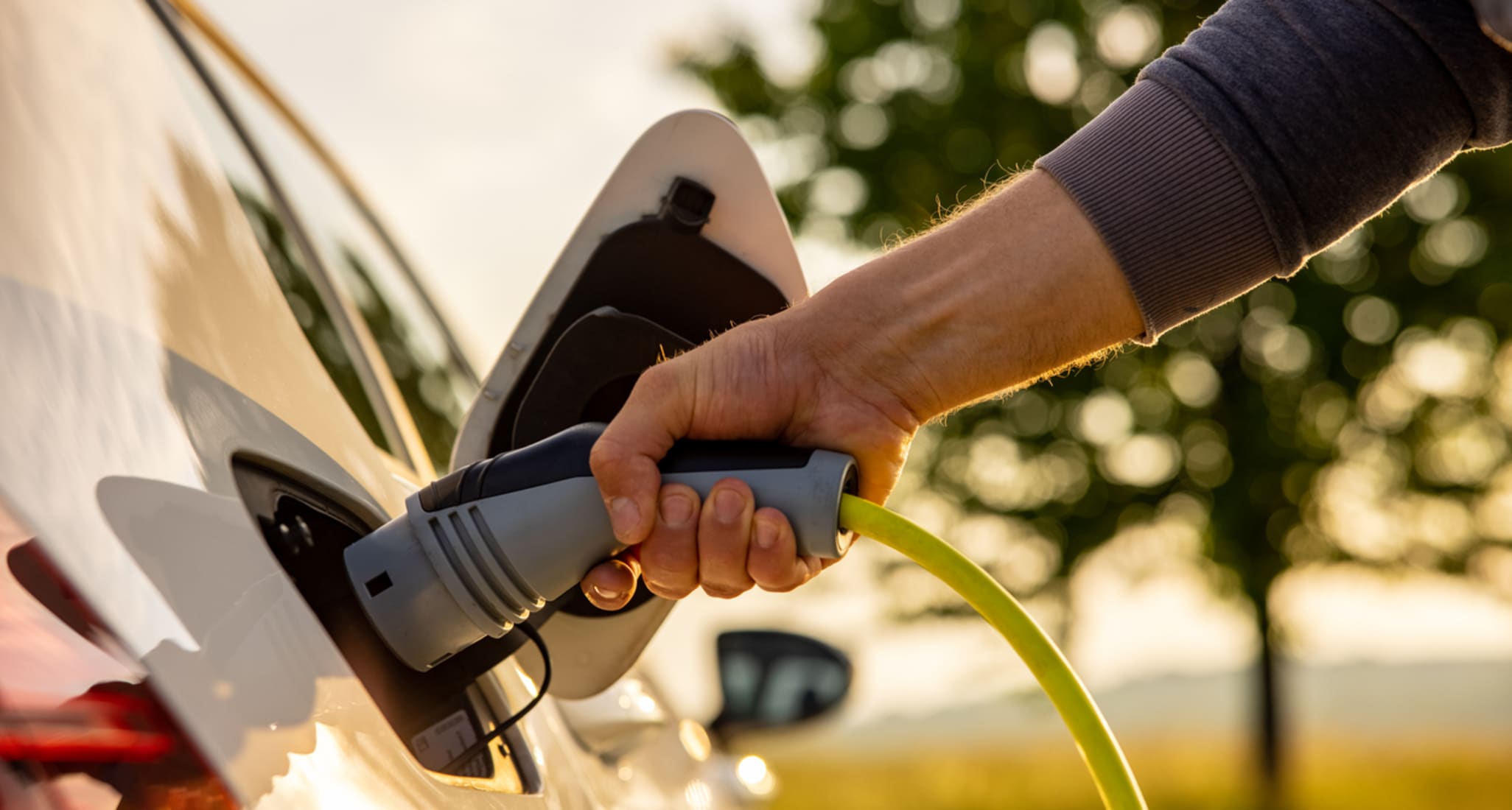 Mann steckt ein Netzkabel in ein Elektroauto zum Laden.