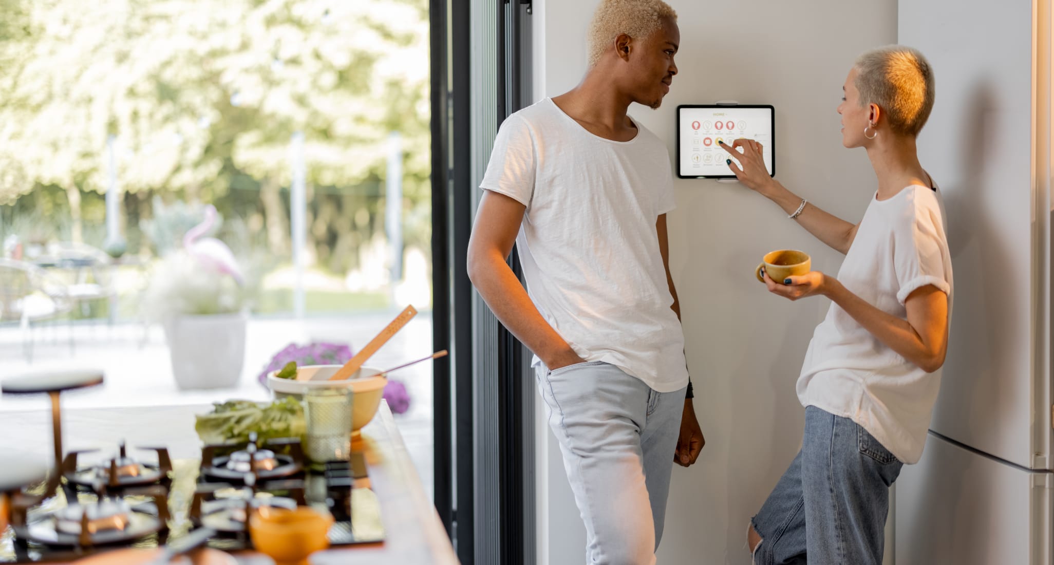 A couple standing in front of the control display of their smart home. The woman is using it.