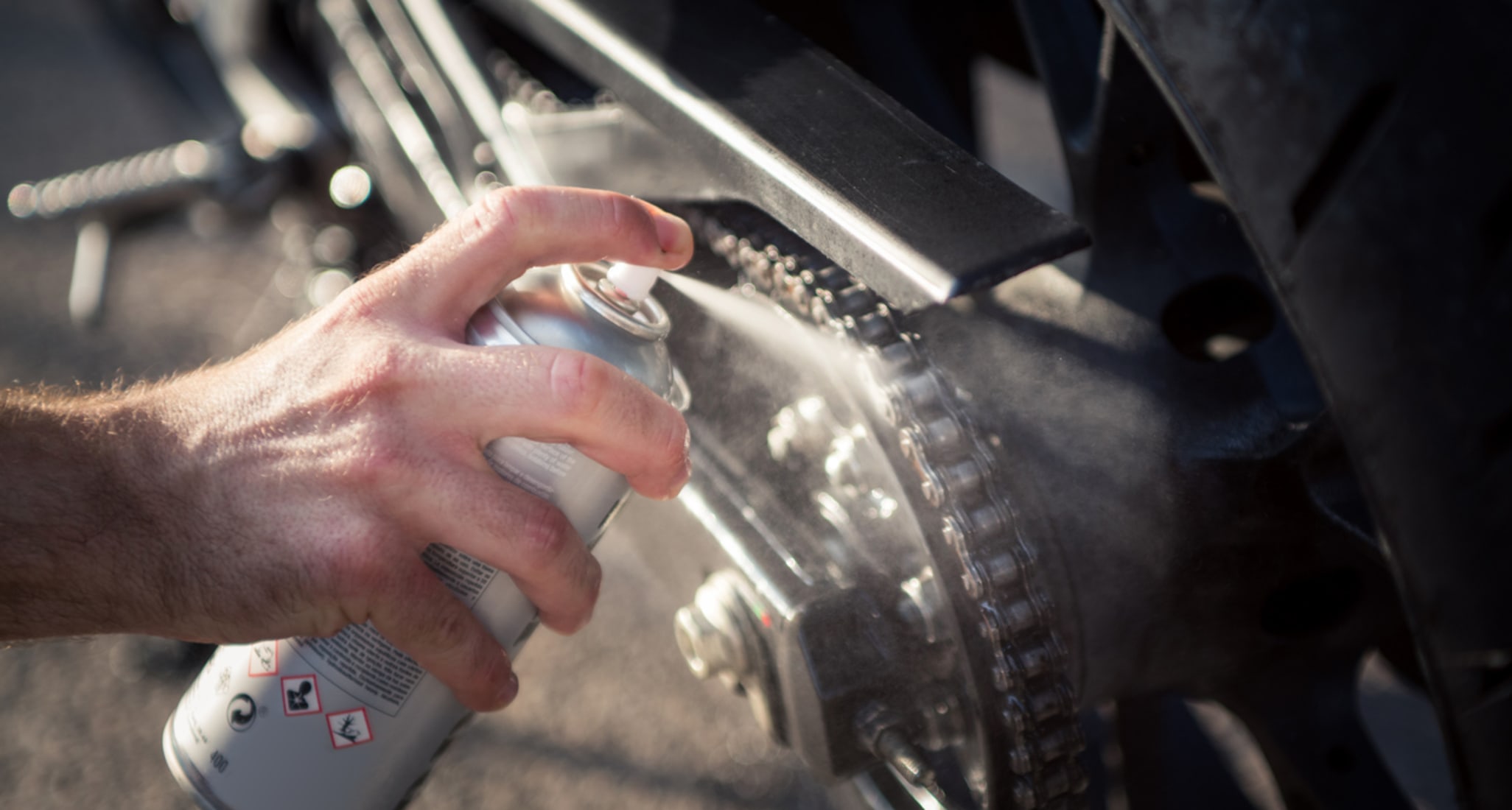 Un uomo olia la catena della moto ed effettua il controllo primaverile.