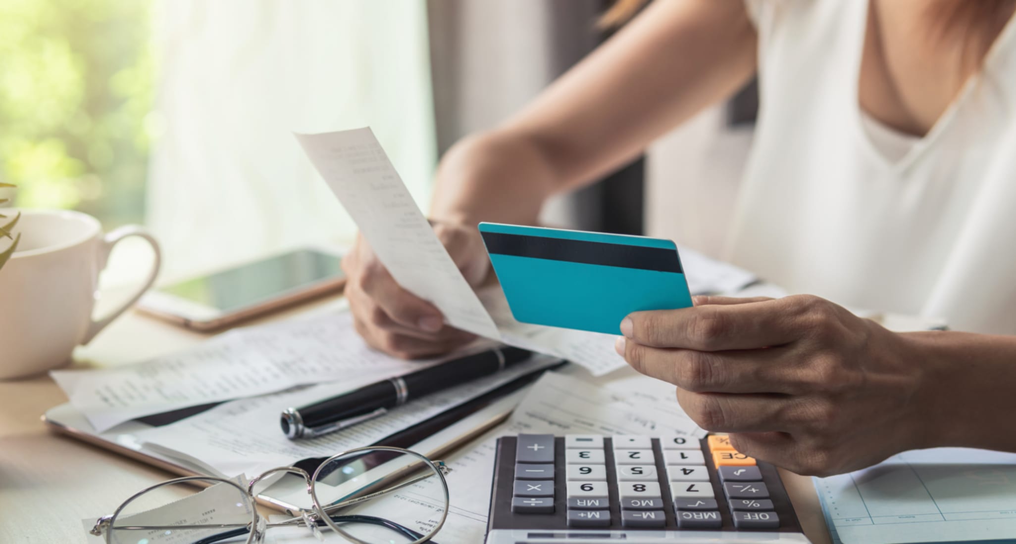 A woman sits at a desk. She has a credit card in one hand, and an invoice in the other.