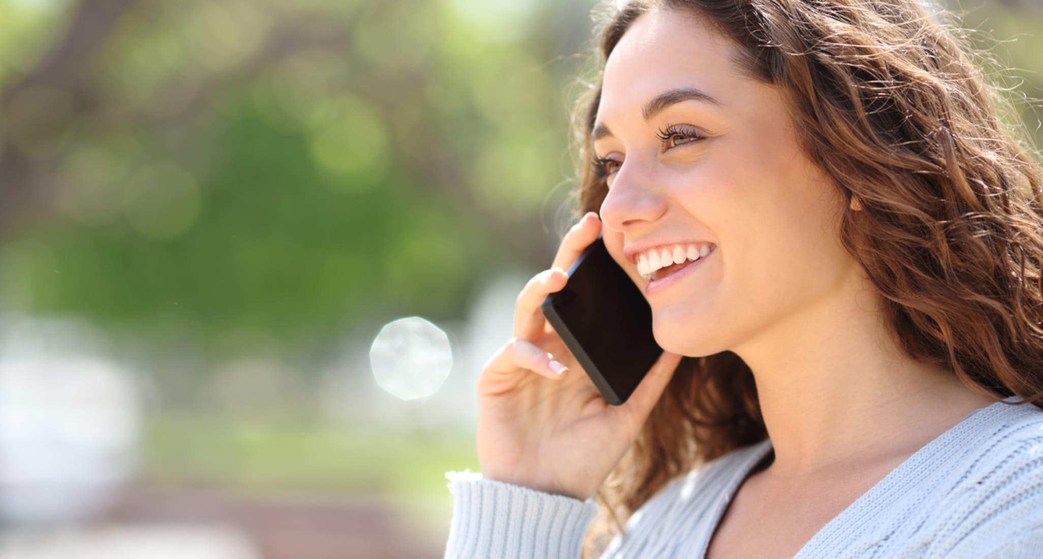 A woman smiling on the phone in the countryside.