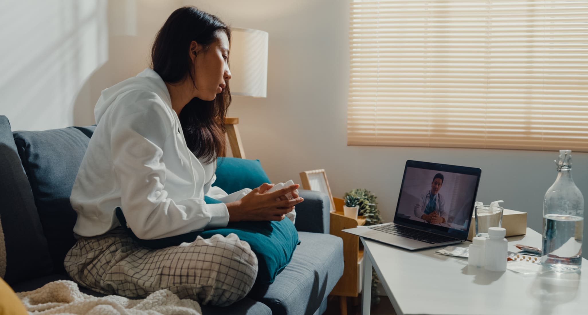 Eine rkanke Frau sitzt vor dem Laptop und redet online mit einem Arzt.