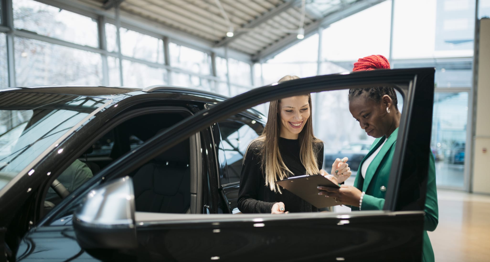 Junge Frau kauft ihr erstes Auto bei Autohändlerin in einer Autogarage.