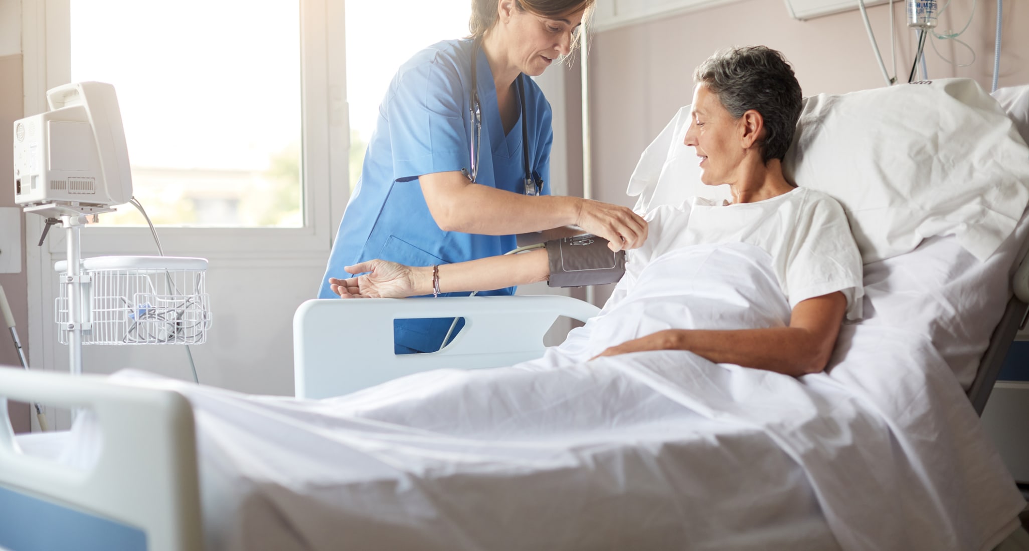 A nurse helping a patient in a hospital bed explaining basic insurance benefits.