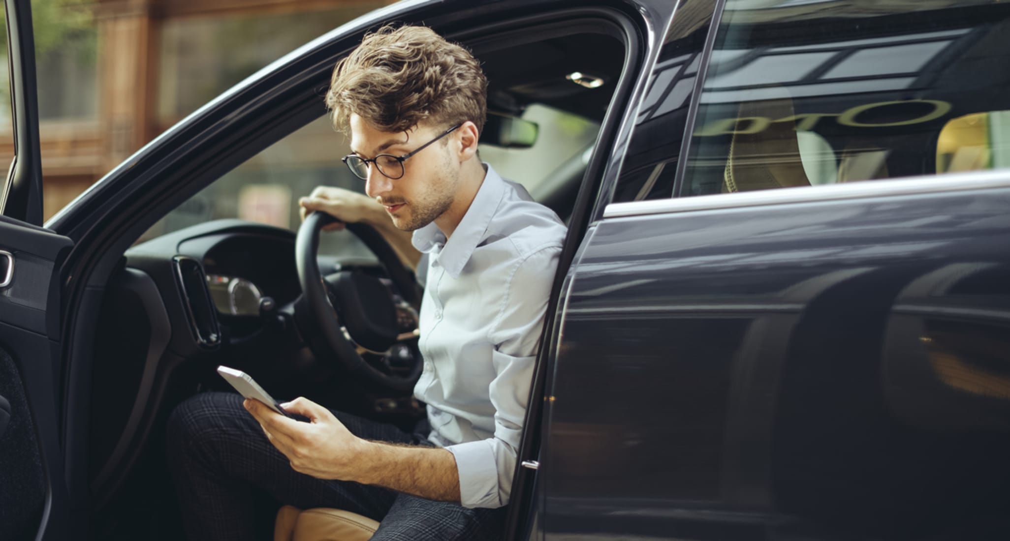 Un jeune homme sort de la voiture et regarde son téléphone portable.