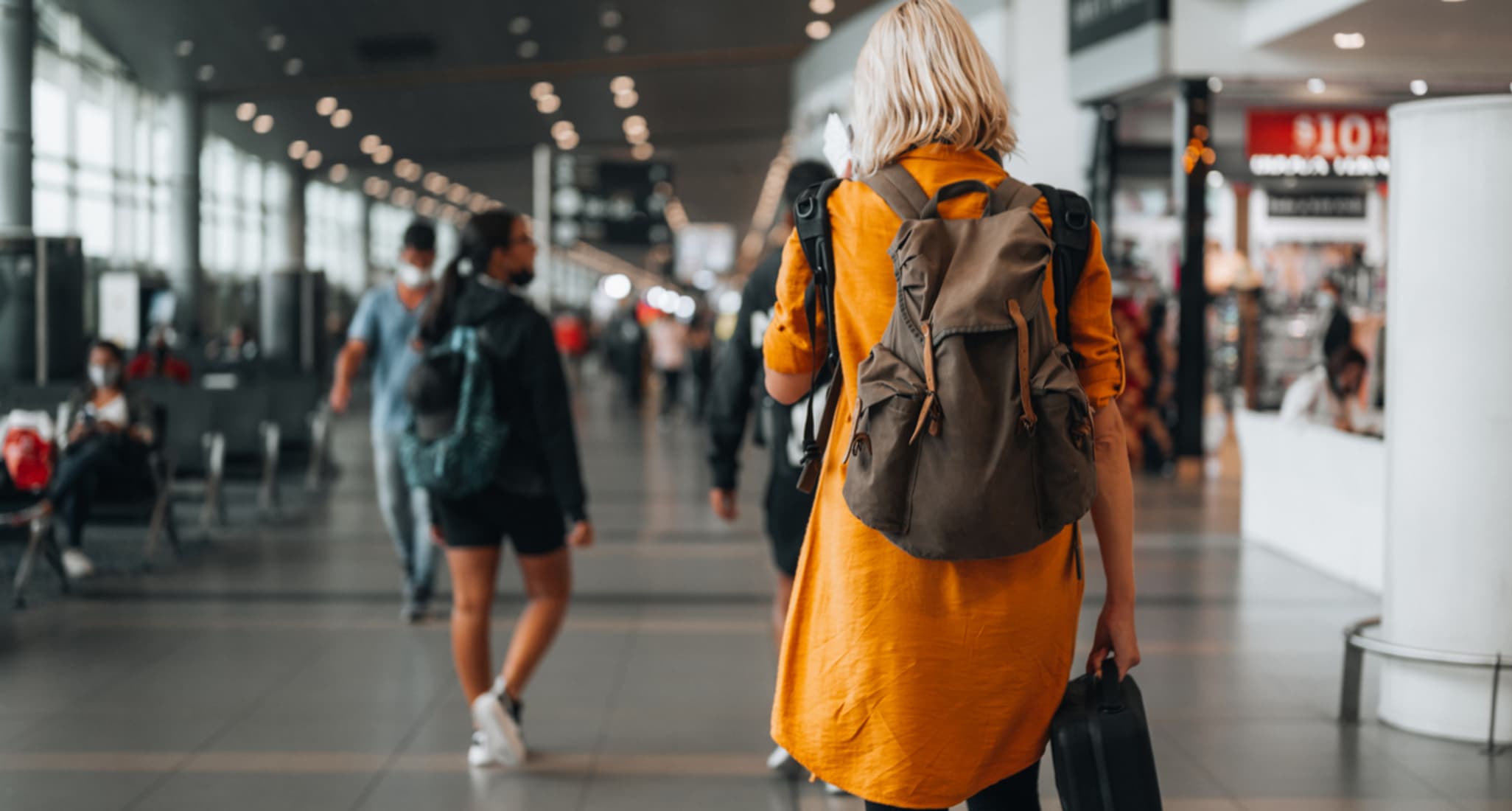 Eine Frau mit gelber Jacke geht am Flughafen zu ihrem Gate.