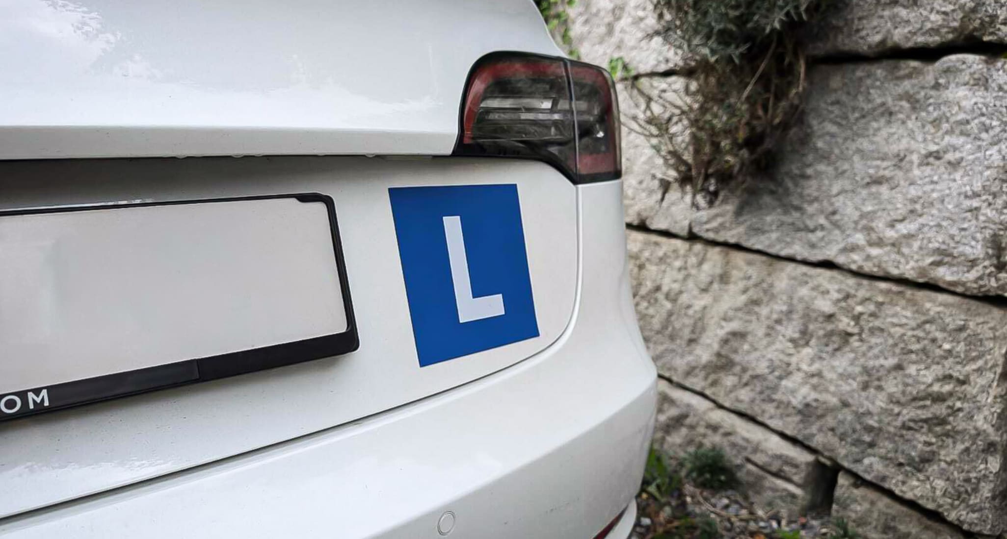 A blue L plate on a white car.