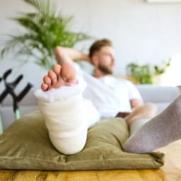 Ein junger Mann mit gebrochenem Fuss sitzt auf dem Sofa.